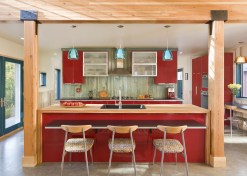 A straight-on view of The Red Cottage's kitchen shows off shiny red cabinets and glulam beam framing, and a playful use of color and materials..