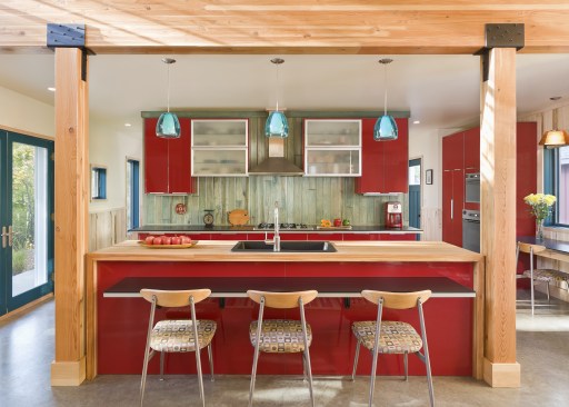 A straight-on view of The Red Cottage's kitchen shows off shiny red cabinets and glulam beam framing, and a playful use of color and materials.. 