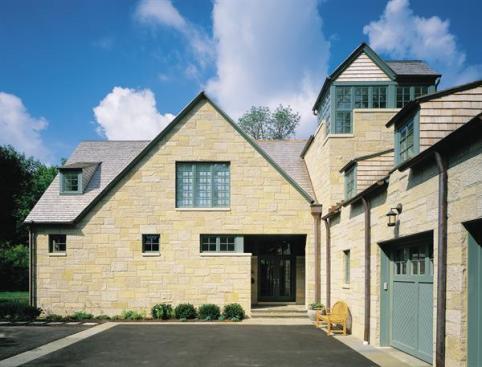 Gables, dormers, and a corner tower lend the limestone-clad home a storybook quality. A recessed front entry reinforces the impression of comfort and protection.