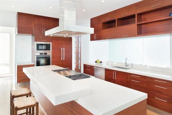 The+island+with+the+cooktop+has+an+extra+slab+of+quartz+composite%2c+a+sculptural+element+that+separates+the+seating+from+the+prep+area