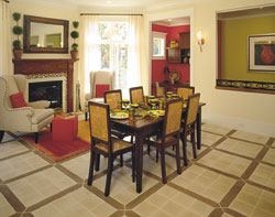 The keeping room features a fireplace detailed with mosaic and copper tiles and highly styled contemporary lighting. The rich wood details on the fireplace surround come from the fictional floor of the "first house," which was "replaced" with concrete tiles resembling wood pickets with limestone inserts.