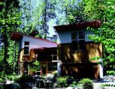 FAIR STRIPES: Vertical battens on the home's plywood siding correspond to the orientation of the surrounding trees.  The upper levels of the homes' two halves are clad in galvanized corugated steel.  Rafters are left exposed in the deep overhangs of a red metal roof.