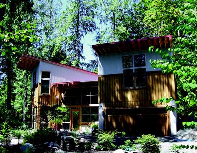 FAIR STRIPES: Vertical battens on the home's plywood siding correspond to the orientation of the surrounding trees.  The upper levels of the homes' two halves are clad in galvanized corugated steel.  Rafters are left exposed in the deep overhangs of a red metal roof.