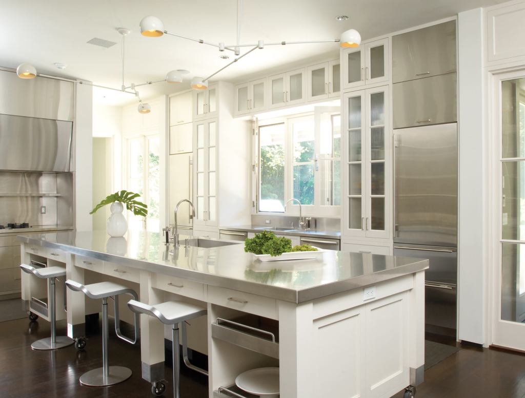 Ebonized walnut floors highlight the kitchen's white woodwork and stainless steel surfaces. The room's extra-tall cabinets, mobile island, and a separate pantry supply ample storage space, while French doors at either end let in natural light and breezes.