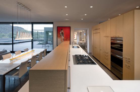 Custom kitchen cabinets in rift-sawn white oak generate a minimalist backdrop for the natural finery framed by careful window and door placement. The kitchen’s pale hues blend with the desert colors.