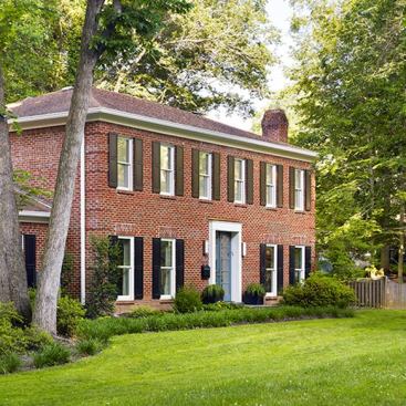 The center-plan colonial, a cooky-cutter home from the 1980s, was enlivened by the design team. The front door and fan window were removed and the brick was filled in. Replacing the front door are more amply sized contemporary-looking doors that admit more light in.