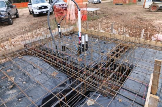 After slab pad is compacted we dig beams and install a vapor barrier and a ton of rebar. Note the rebar above slab for a house board-formed wall post-pour.