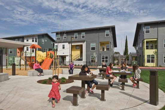Parking is tucked under and behind buildings, leaving the central open space for a playground and picnic tables.