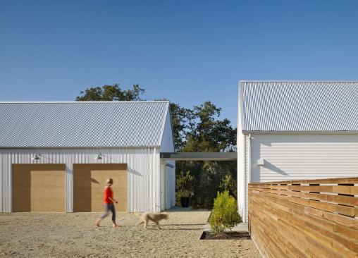 The garage is the “barn” in this complex of farm-like buildings, so it’s clad in a different material from the house. Vertically installed white corrugated metal siding is not only a subtle departure from the white Hardipanel on the residential buildings, it also helps break down the scale.