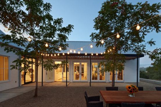 The gravel courtyard is filled in with a small grove of shade trees that lose their leaves in winter, allowing for passive solar heating.