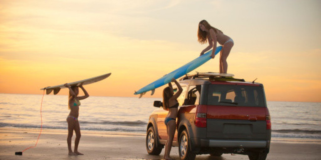 girls at beach putting surfboards on car top