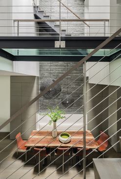 A narrow wall of stone masonry rises the full height of the atrium, forming a backdrop for the dining area and lending a textured surface for light to play across.