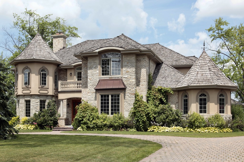 Luxury stone home with turret and cedar shake roof.