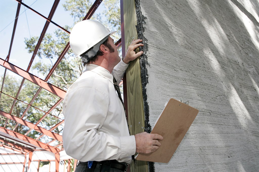 A building inspector checking over incomplete stucco work on new construction. Focus on stucco work.
