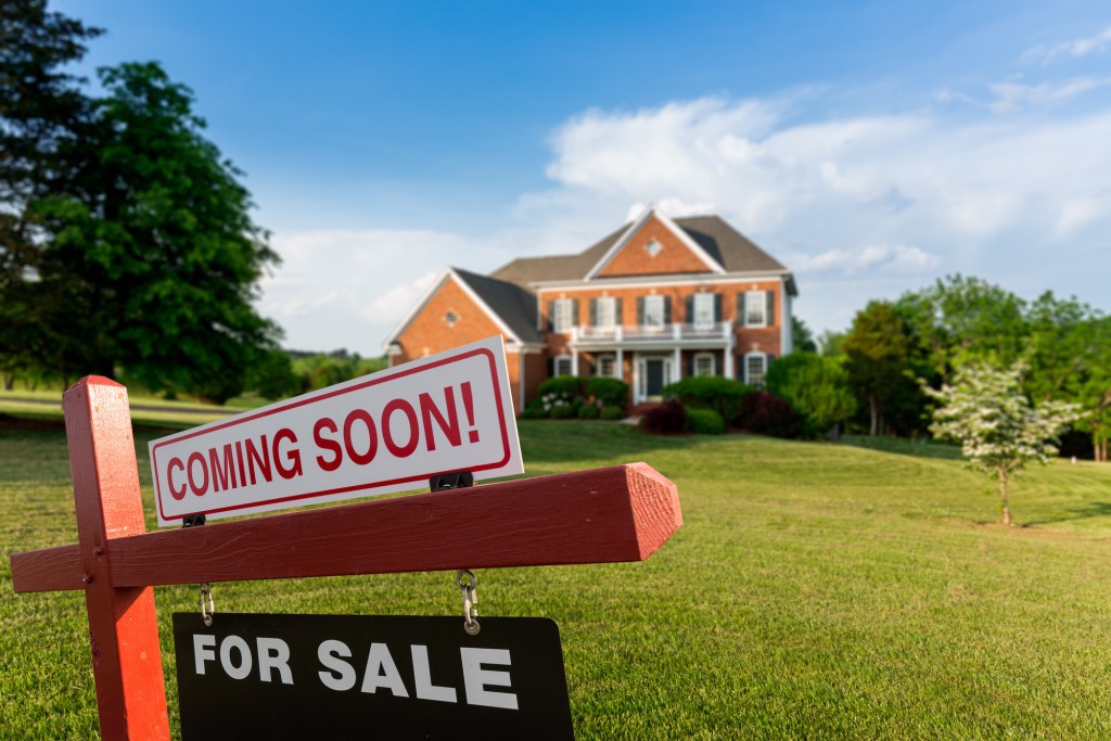 For Sale and Coming Soon realtor sign in front of large brick single family house in expansive grass yard for real estate opportunity