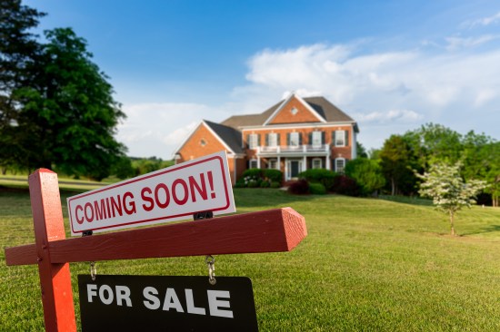 For Sale and Coming Soon realtor sign in front of large brick single family house in expansive grass yard for real estate opportunity