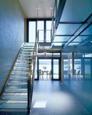 The glass stair doubles as artwork in the house's central gallery. Its reflective translucency scoops light into the deepest part of the structure, and a steel rod suspension system eliminates obtrusive columns.