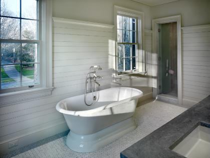 The antique oak vanity, custom-built to resemble furniture, as well as the wainscoting, tumbled marble floor laid in a basket weave pattern, and soapstone countertop and backsplash help connect the design to the 1930s-era home.