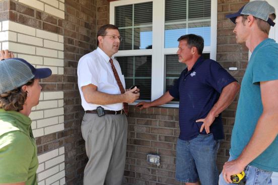 Tom Mayberry (dark blue shirt) and his sons Jake (light blue shirt) and Jason(green shirt) meet with Chaplain Todd Decker (white shirt with tie) at the site of his destroyed rental home which has been rebuilt by the Mayberrys.