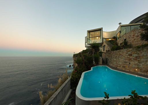 The three layers of structure above the pool terrace comprise a stone retaining wall, the stone-clad lower level, and the stuccoed upper level.