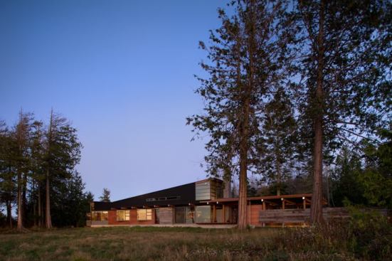 Spanning one end of a forest-framed meadow and oriented to Western views of the Olympic Islands, Bohlin Cywinski Jackson's Port Townsend Residence is a long, slender structure primarily made of exposed steel, wood columns, wood beams and rafters, and reclaimed barnwood. The variety of materials used help reduce the building's scale and define each volume.