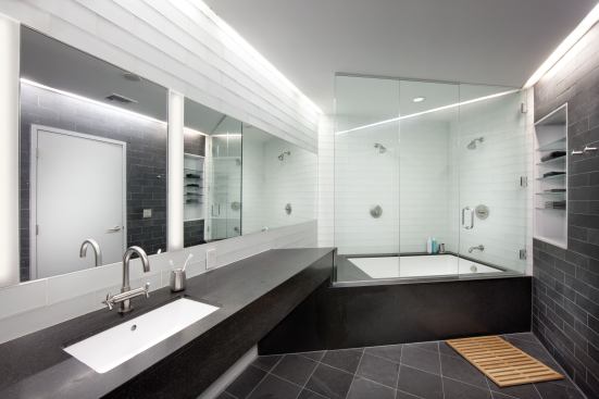 The husband’s bathroom continues the angular lines as the space features a honed granite vanity and tub surround, dark gray slate floors, and frosted glass wall tiles.
