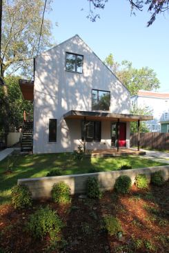 Clad in cedar shingles and a standing-seam metal roof, the house features a narrow driveway and a small front porch leading to the owner’s unit.