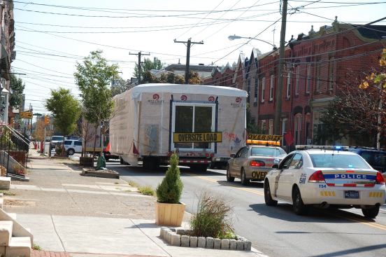 Escort Service. A wide-load module being transported through Philadelphia is trailed by police cars to avoid vehicular mishaps.