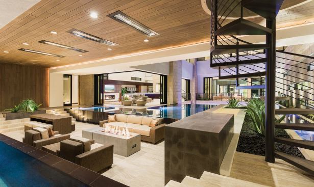 A novel entertainment space, complete with a TV and gas-powered firepit, casual seating, and a dining area, sits between two zero-edge pools that cascade into perimeter troughs. The area peeks into the great room and kitchen, while a spiral stair behind the TV niche leads to an open-air balcony above. The ability to engage with and enjoy the outdoor areas is directly attributable to the 90-degree corner patio doors from Sierra Pacific, which telescope into each other and then pocket away to create a full reveal. Natural limestone flooring from Daltile is the home’s prevailing floor finish, but look up in this area, the kitchen-great room, the foyer, and a few other spaces around the house to see an engineered wood plank from Mohawk Industries used as a warm and welcoming ceiling finish.