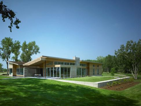 The butterfly roof satisfies the subdivision’s minimum-slope requirement, though perhaps not in the way the document’s drafters anticipated. A level section of yard retained by a low concrete wall serves as a green deck.