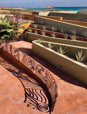 Large doors open to curving terraces covered in palapa, or palm fronds, tied down with fish netting. Flanked by spiky agave and sculptural railings, the ramp becomes a stroll in the garden