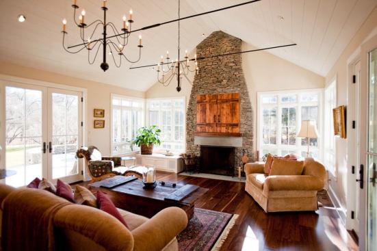 The living area continues the theme with many of the same finishes as the kitchen, including the wrought-iron chandeliers and visible iron ceiling ties. The stacked stone fireplace and chimney provide a focal point in the light-filled room and house the family's flat-screen television, which is concealed behind hayloft doors milled from reclaimed barn wood. The hayloft doors are an element in every bedroom with a television, as well.