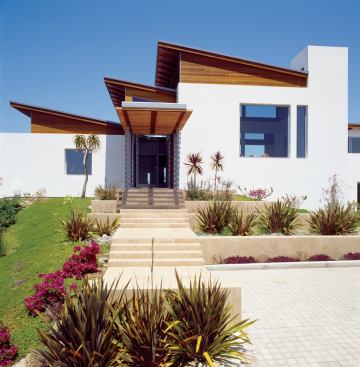 The home's front entrance leads through multiple interior levels to a series of side and rear terraces defined by whitewashed stucco walls.
