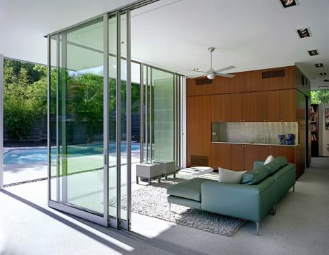 Sapele veneer wraps the pavilion's wet core, which contains the kitchenette (shown), Murphy bed on the opposite side, and bathroom inside. Floor-to-ceiling sliding doors stack to open the space to the terrace.
