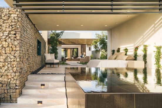The master suite exemplifies the layering of living spaces and features found throughout the house. From a private patio, a deep, zero-edge spa graces an open-air sleeping porch and a quiet courtyard bordered by a retaining wall of regional rocks that add texture and subtle color.