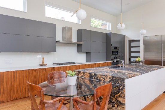 Above a continuous row of natural walnut cabinets are minimalist gray cabinets. The island features  a  Sedna countertop with waterfall edge.