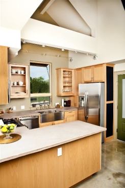 Double-height interiors, polished concrete floors, and energy-efficient appliances highlight the kitchens and dining spaces.