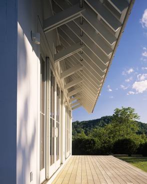 A deep porch roof keeps summertime sun from heating up the first-floor interiors. A simple, galvanized steel pipe ties together the rafter tails and brackets.