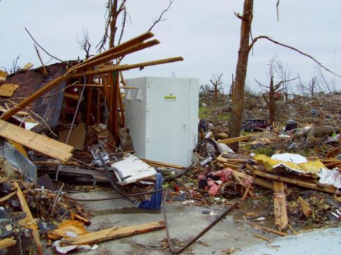 An intact Twister Safe tornado shelter next to a destroyed house.