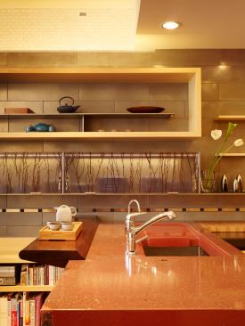 Perpendicular to the cooktop area are the sink and drainboard. The red surface is made of Geocrete, one of the trademarked concrete blends that Cheng is known for. The concrete slopes gently to meet the walnut shelf, preventing water from pooling or from seeping into the joints.