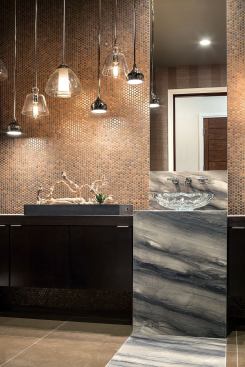 The first-floor powder room shines with a pressed copper backsplash from Daltile and metal pendant lights hung at staggered heights. The energy-efficient LED fixtures are from Progress Lighting.