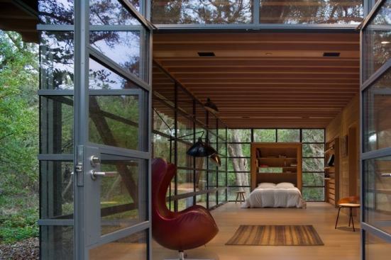 Full-height glazed walls make up both outbuildings' rear volumes, opening their interiors to views of the creek banks. The exposed Douglas fir rafters extend through the living and working spaces to the exterior of each glass box, drawing the eye toward the outdoors. A shared gravel courtyard connects the two outbuildings.