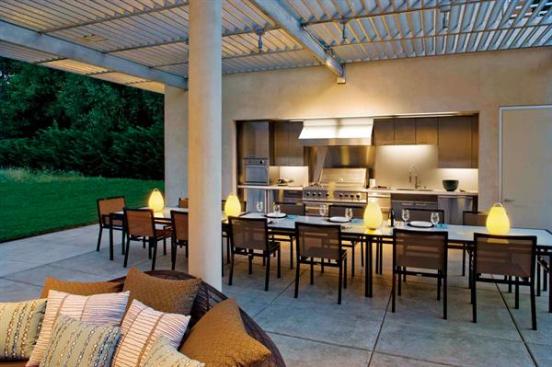 The metal overhead grid shades the kitchen and edges of the east/west-oriented pavilion, its slats angled to block direct sun during the day.