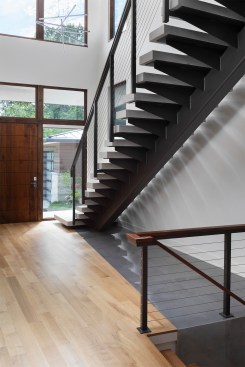 The Foyer features white oak flooring in the direction of the lake views. The polished ceramic tile beneath the stair mimics water and flows with a waterfall edge drawing you down to the lower level. The floating Lannon stone stair and cable railing preserve the design’s transparency to maximize views through to the lake. 