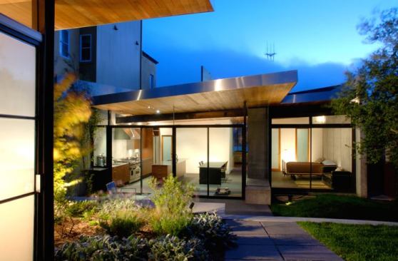 A concrete wall forms each sidewall of the house and extends beyond the interior footprint to enclose a private garden, visually and physically accessible through the walls of sliding glass doors in the adjacent kitchen/living room and bedroom.