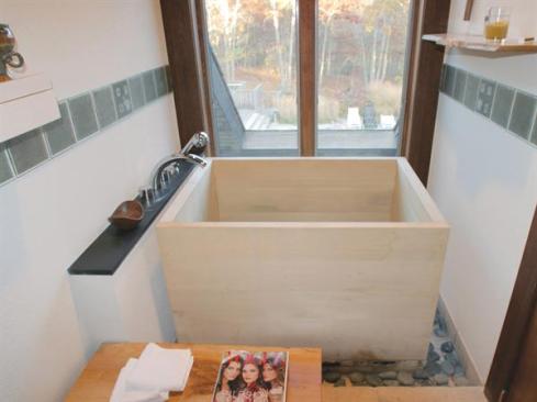 A line of green glass tiles, positioned at head height for bathers, creates an appealing visual break in the tall white walls and helps bounce light around the tight space.