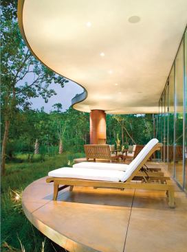 The undulating shape of the first-floor terrace creates a soft, floating edge where the house meets the landscape. The chimney of the copper-clad outdoor fireplace rises through the matching second-story overhang.