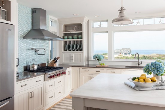 White cabinets make this kitchen feel modern, but the blue-tiled backsplash adds vibrancy to the space. Large windows flood this beach-side kitchen with natural light. Project: Cape Cod Beach House by REEF 