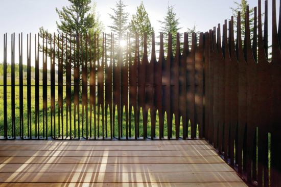 The steel fence is composed of slender fins that are angled at varying degrees. The fins split into forks that graduate from short to long. Those subtle moves make the fence appear to undulate as you walk around it and also alters the levels of transparency. 