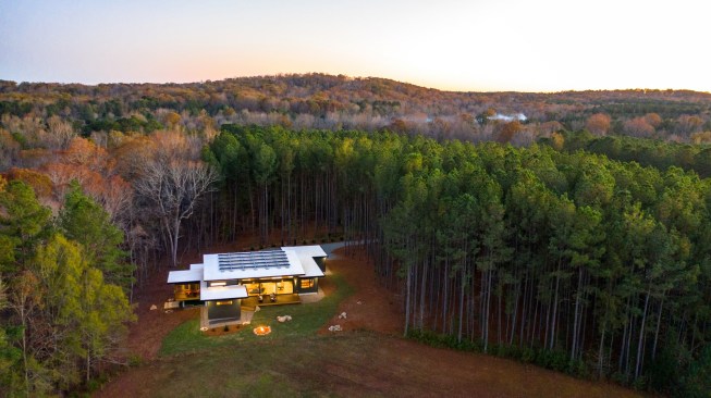 An aerial view shows the house in context and the array of solar panels on the flat roof's white cool-roof membrane.